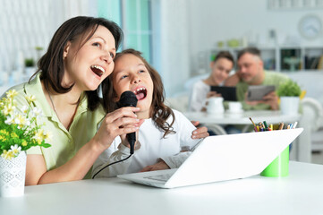 Emotional mother and daughter singing karaoke with laptop at home