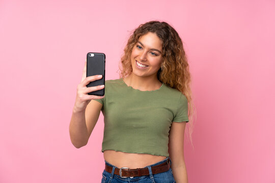 Young blonde woman with curly hair isolated on pink background making a selfie
