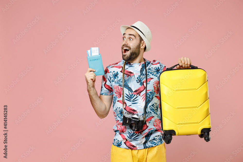 Wall mural Shocked young traveler tourist man in summer clothes hat photo camera hold suitcase passport ticket looking aside isolated on pink background. Passenger travel on weekend. Air flight journey concept.