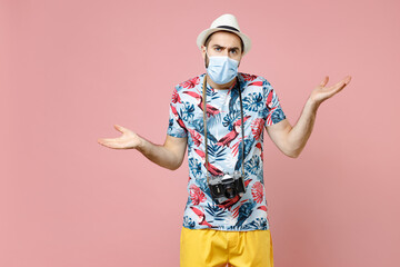 Worried young traveler tourist man in face mask to safe from coronavirus virus covid-19 spreading hands isolated on pink background studio. Passenger traveling on weekends. Air flight journey concept.