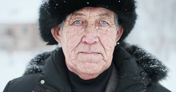 Old man's portrait. Close up outdoor portrait of the old man with wrinkles and deep blue eyes wearing black winter hat and looking into the camera