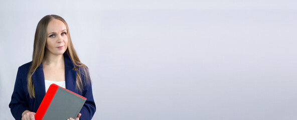 Obraz premium Businesslike, beautiful, caucasian girl. She is standing on a light background, looking at the camera.She's holding a tablet computer, wearing a blue jacket and white blouse, and has long blonde hair.