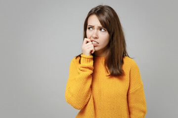 Young thoughtful overthinking pensive attractive troubled woman 20s wearing casual knitted yellow sweater looking aside biting lips nails fingers isolated on grey color background studio portrait