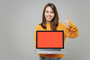 Young smiling freelancer copywriter cute woman 20s in knitted yellow sweater hold laptop pc...