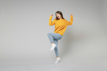 Full length of young smiling excited happy woman 20s wearing yellow sweater walk going do winner...