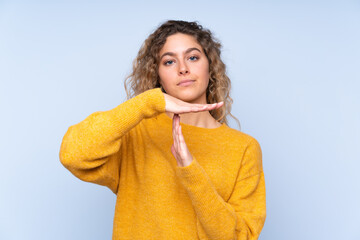 Young blonde woman with curly hair isolated on blue background making time out gesture