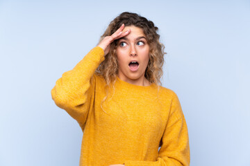 Young blonde woman with curly hair isolated on blue background has just realized something and has intending the solution