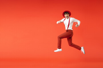 Fototapeta na wymiar Full length of young spanish latinos smiling cheerful overjoyed fun man 20s wearing hat white shirt trousers, suspenders jump high running fast speed isolated on red color background studio portrait.