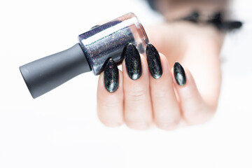 Female hand with long nails and gray black manicure with bottles of nail polish
