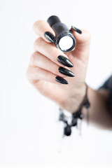 Female hand with long nails and gray black manicure with bottles of nail polish