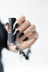 Female hand with long nails and gray black manicure with bottles of nail polish