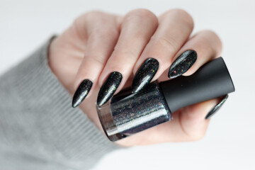 Female hand with long nails and gray black manicure with bottles of nail polish