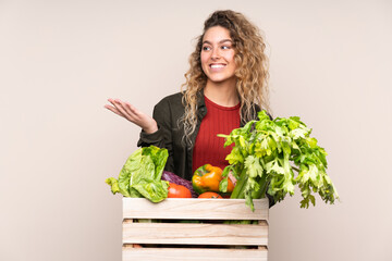 Farmer with freshly picked vegetables in a box isolated on beige background holding copyspace imaginary on the palm