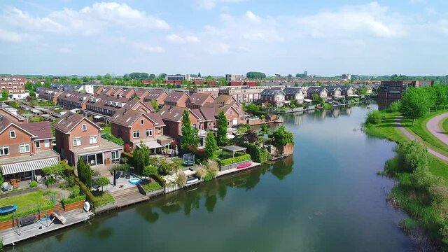 Drone flying upward over the beautiful suburb of Rotterdam in the Netherlands, the neat buildings surrounded by green trees and a river