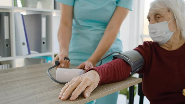 Old woman measuring blood pressure using tonometer during appointment with doctor