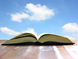 book open on wood table with beauty blue sky white cloud  background