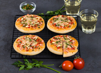 Italian mini pizzas with sausage, pickles, tomatoes, mozzarella, parsley, greens on a metal stand on a dark gray background