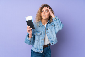 Young blonde woman with curly hair isolated on purple background in vacation with passport and...