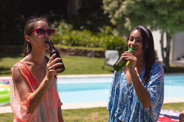 Two mixed race female friends drinking at a pool party