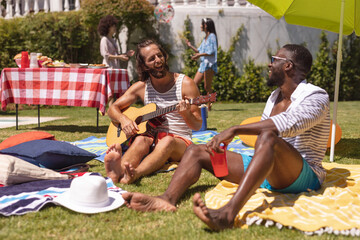 Two diverse male friends playing guitar and smiling at a pool party
