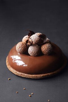 Contemporary Chocolate Mousse Cake with Craquelin Choux Pastry, covered with chocolate mirror glaze, on a dark background.