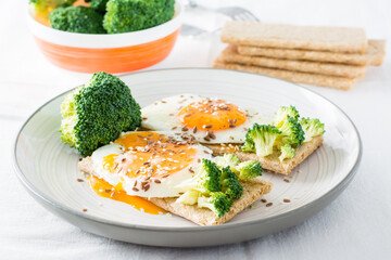 Bruschetta with scrambled eggs and broccoli on a grain crispbread with sesame seeds and flaxseed on a plate and a bowl of broccoli on the table