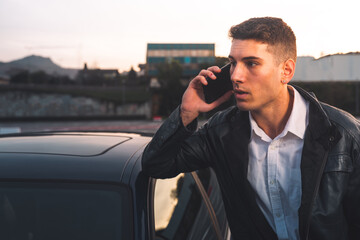 Young caucasian man using a smartphone with a sports car behind