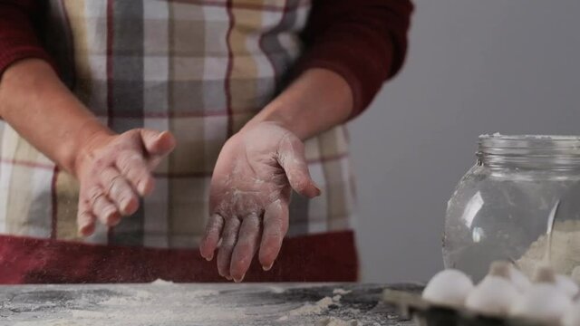 Woman in culinary apron shaking flour from hands after baking, slow motion