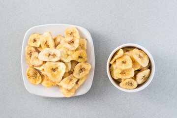 Baked banana chips in a white bowl and saucer on the table. Fast food. Web banner. Top view