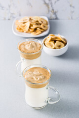 Quarantine trendy cuisine. Two cups with dalgona coffee and banana chips on a gray background. Vertical view