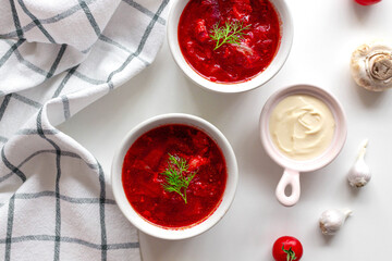 Top view of the traditional Ukrainian borscht or soup with beets, potatoes, tomatoes, meat in bowls on white background. Top view. Free copy space.