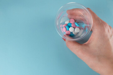 Medicine and pills. Female hand holding pills in small plastic medicine cup. Multi-colored medicines on the pastel blue background.