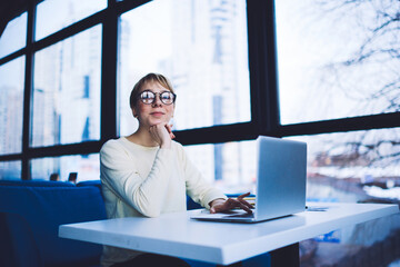 Smiling woman with hand at chin using laptop