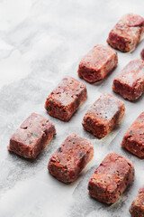 Composition with raw square cutlets on light background. Natural food for dogs. BARF dog diet