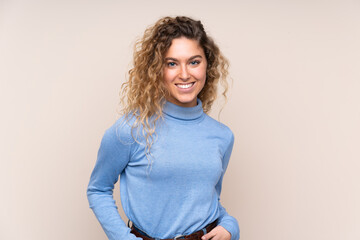 Young blonde woman with curly hair wearing a turtleneck sweater isolated on beige background...