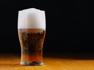 Pint glass of light lager beer on wooden table and dark background. Copy space