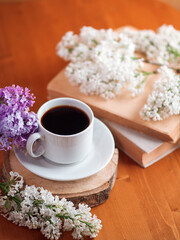 Obraz na płótnie Canvas Spring mood, a cup of aromatic espresso coffee on a wooden table, branches of blooming lilac and a book