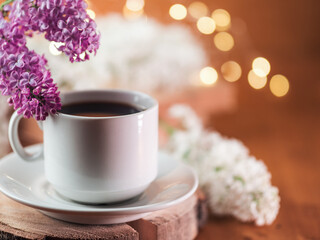 white coffee cup on wooden table with blooming lilac branches and copy space