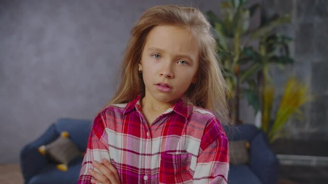 Emotionally stressed sulking adorable preadolescent girl standing with arms crossed, sighing heavily, looking with sad expression , feeling disappointment, resentment and hopelessness indoor