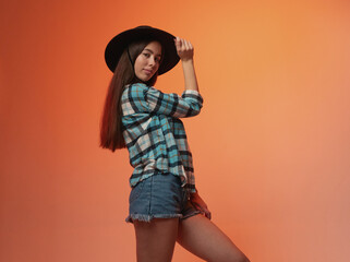 Girl in plaid shirt and cowboy hat on orange background