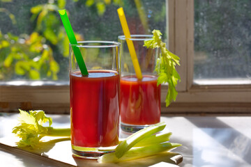 Freshly prepared tomato juice with a celery branch in two glasses stands on the kitchen table by the window. Detox snack. Horizontally.