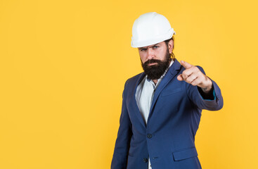 serious man with beard wear hard hat pointing finger. engineering. architecture and building. male builder wearing formal suit and helmet for protection. working on construction project. copy space