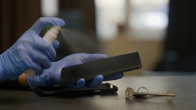 View of smartphone disinfection. Prevent Covid-19 spreading. Process of spraying desinfectant on phone screen. Rubber-gloved woman hands. New normal