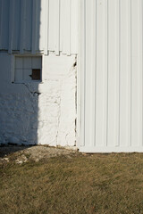 Facade of an old wood and stone barn with window covered over with white paint; a heavy shadow falls on the building