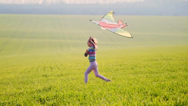little girl playing with colorful kite on green sunny field