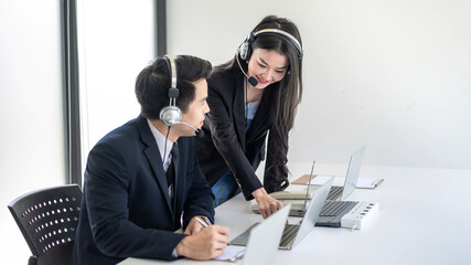 Young man and woman Asian call center workers wearing headphone are working together in the office