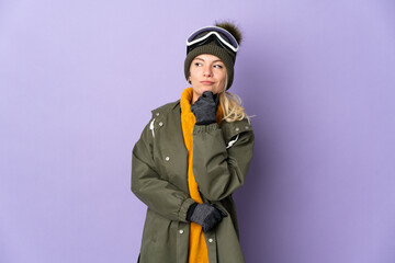 Skier Russian girl with snowboarding glasses isolated on purple background and looking up