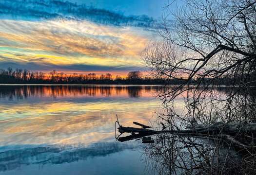 Colorful dramatic lake sunset with cloudy sky and black trees