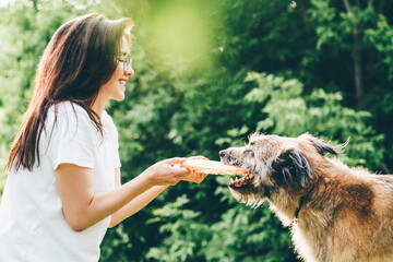 Women playing with dog in the summer park. Cheerful lady with friendly old dog sitting on lush green meadow of public garden on nice day.