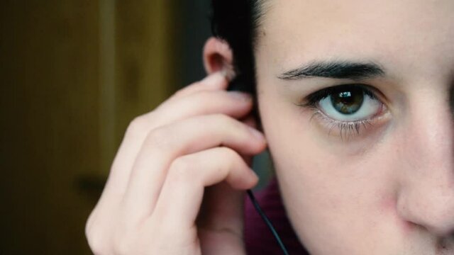 Detalle de una mujer joven poni&eacute;ndose unos auriculares para escuchar m&uacute;sica. Se ve medio rostro, ojos verdes.